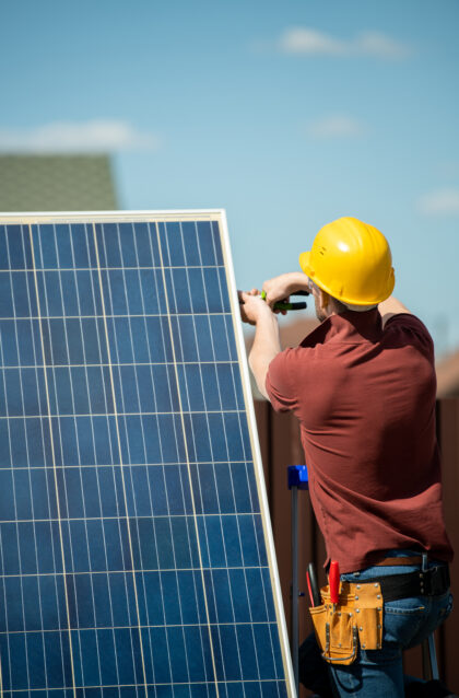 Worker in safety helmet installing photovoltaic panel for customer, view from the back